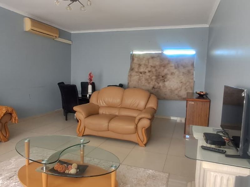 A spacious living room featuring tiled flooring, coving, and a wall-mounted split-system air conditioner.