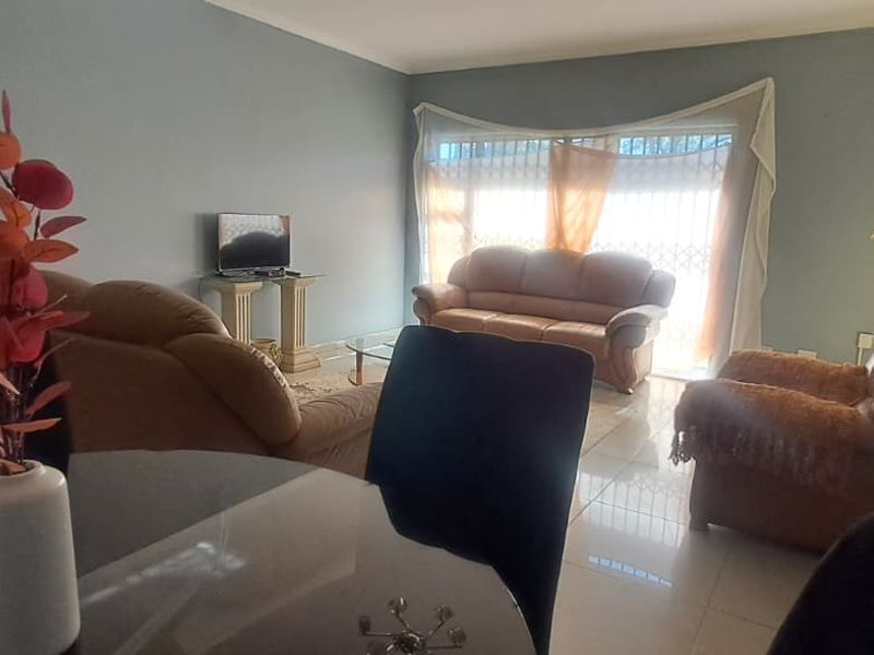A spacious living room featuring tiled flooring and a large window with an integrated security gate, providing natural light to the area.