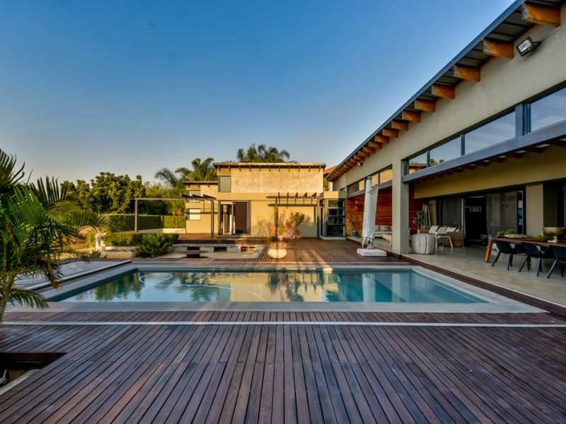 A spacious outdoor entertainment area featuring a swimming pool, extensive timber decking, and a covered patio with exposed timber rafters.