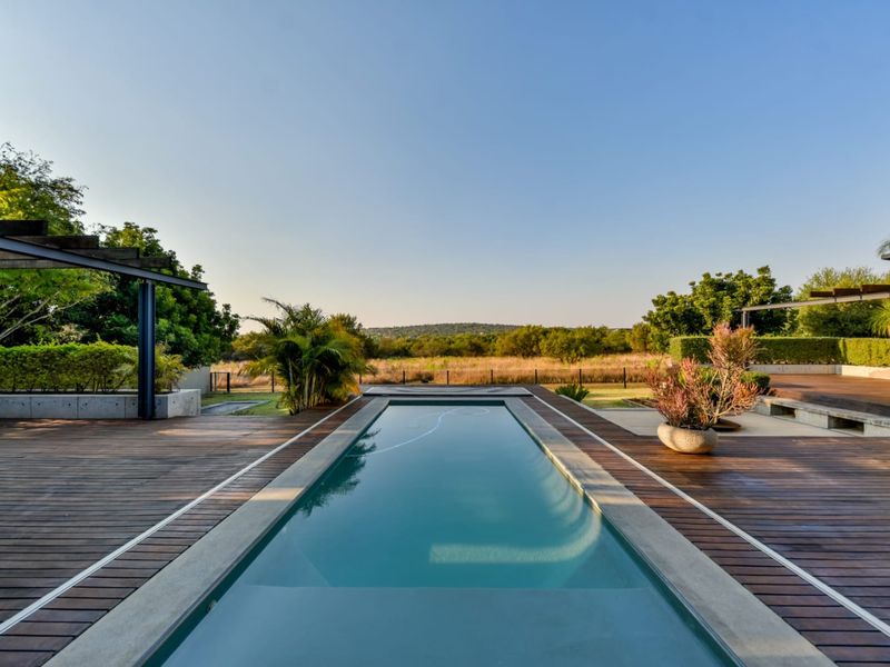 A modern outdoor pool area featuring extensive timber decking, a sleek swimming pool, and a pergola, set against a scenic natural landscape.
