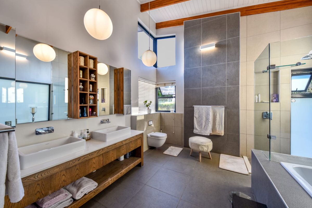 Modern, spacious bathroom featuring a double vanity with vessel sinks, wall-hung toilet, glass-enclosed shower, and a freestanding bathtub under exposed timber ceiling beams.