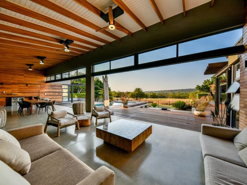 Spacious covered patio featuring polished concrete floors, timber-clad walls, exposed beam ceiling, and seamless indoor-outdoor flow to the pool and garden area.