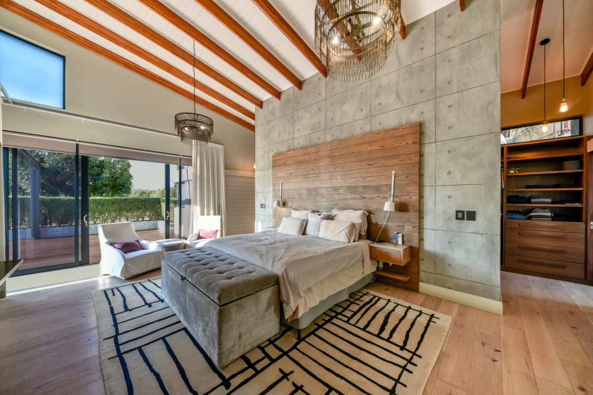 Spacious master bedroom featuring exposed timber beams, a concrete feature wall, hardwood flooring, and direct access to an outdoor patio through sliding glass doors.