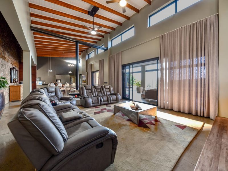 Spacious open-plan living area featuring high ceilings with exposed timber beams, polished concrete floors, a stone feature wall, and large sliding doors to the patio.