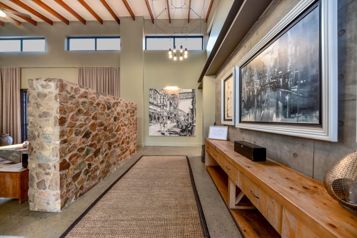 Spacious living area featuring a striking stone feature wall, exposed timber ceiling beams, polished concrete floors, and custom built-in timber cabinetry.