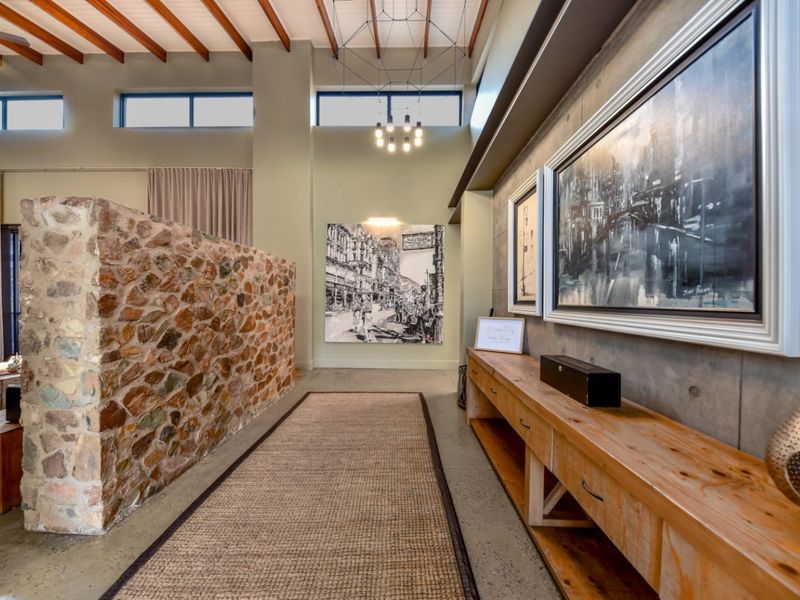Spacious living area featuring a striking stone feature wall, exposed timber ceiling beams, polished concrete floors, and custom built-in timber cabinetry.