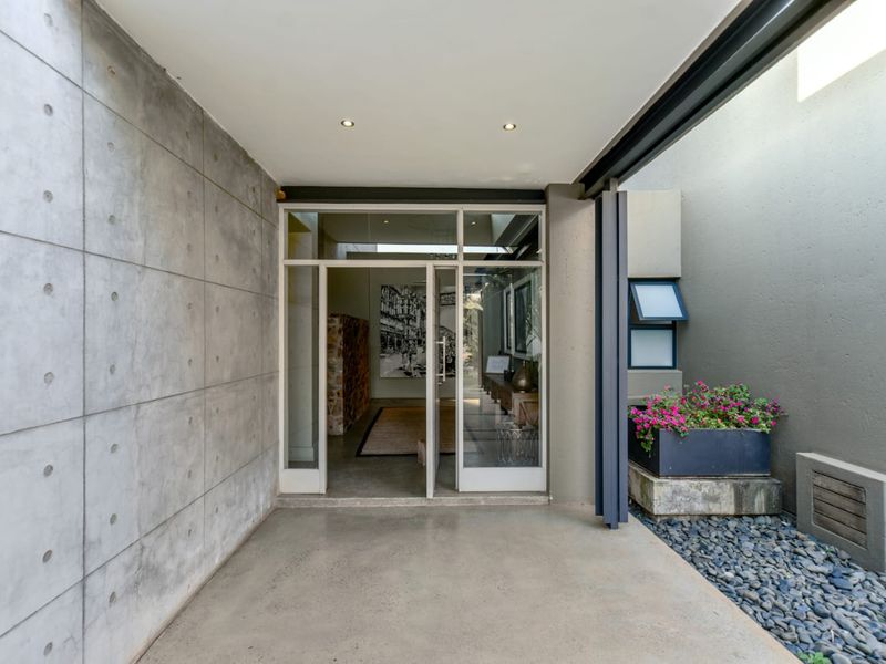 A modern, minimalist entrance featuring exposed concrete walls, polished concrete flooring, and a sleek glass-paneled door with integrated lighting.