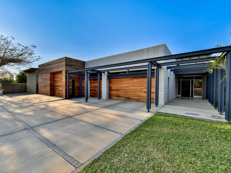 Modern architectural front facade featuring exposed concrete, timber cladding, a steel pergola, and a spacious paved driveway.