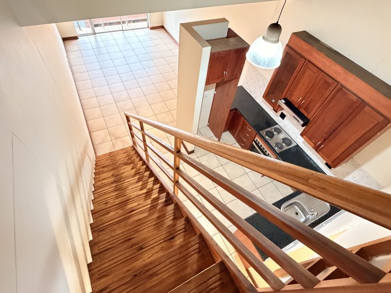 An elevated view of an open-plan apartment featuring a wooden staircase, tiled living area, and a functional kitchen with built-in cabinetry and appliances.
