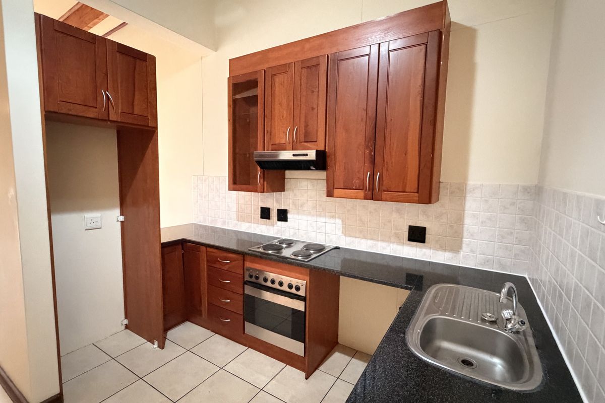 A functional kitchen featuring warm-toned wooden cabinetry, granite countertops, a built-in oven with electric hob, and a stainless steel sink.