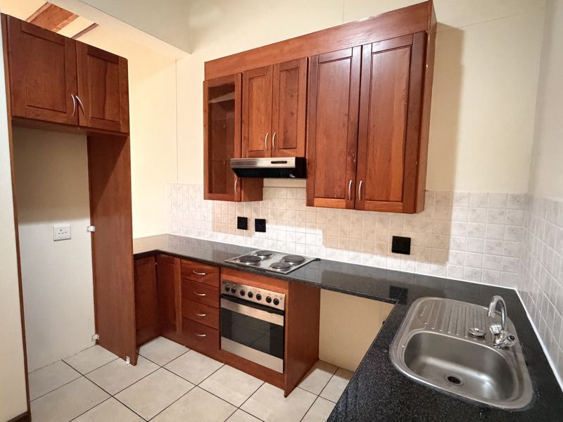 A functional kitchen featuring warm-toned wooden cabinetry, granite countertops, a built-in oven with electric hob, and a stainless steel sink.