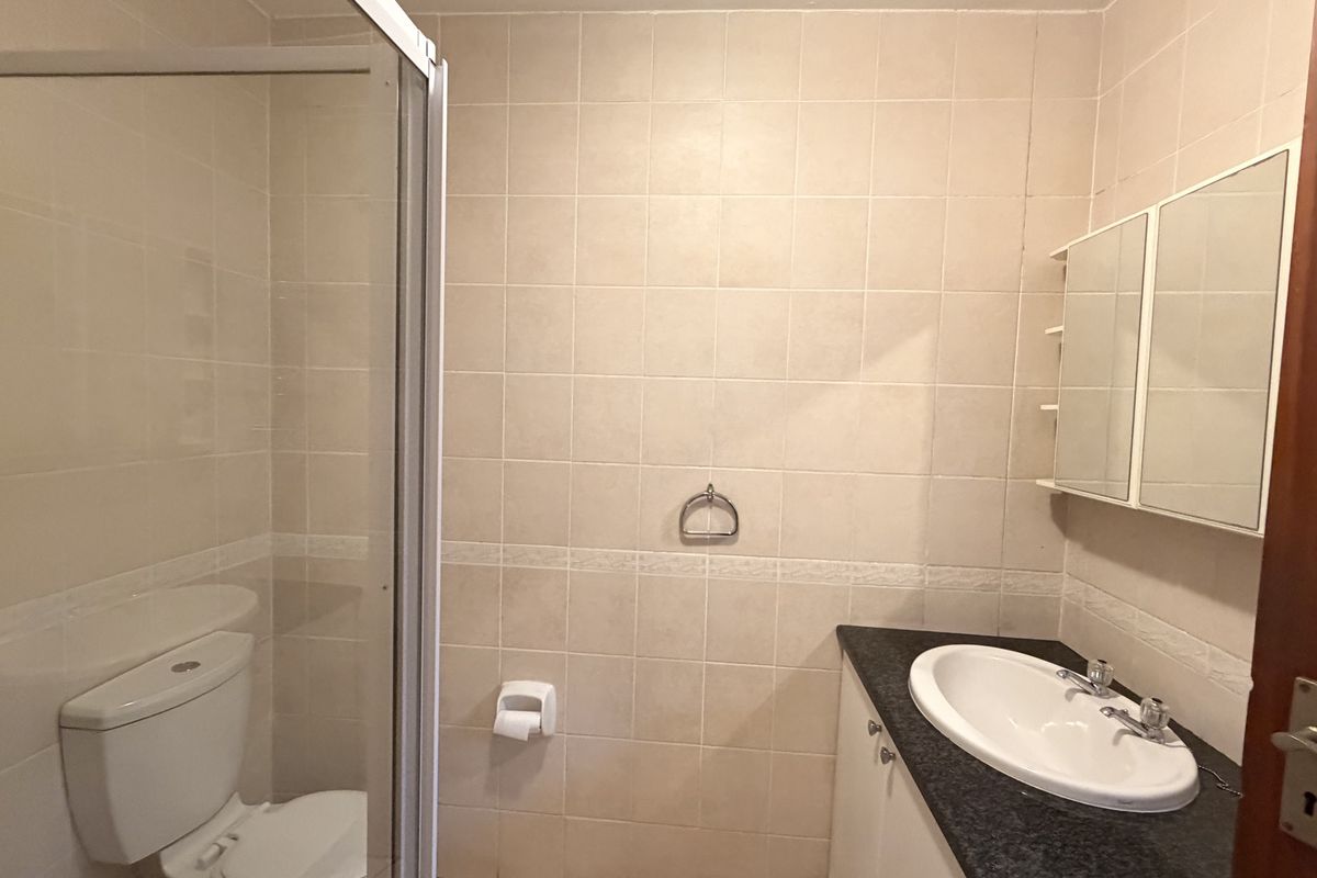 A functional bathroom featuring a shower enclosure, vanity cabinet with basin, and wall-mounted medicine cabinet, finished with neutral wall tiling.