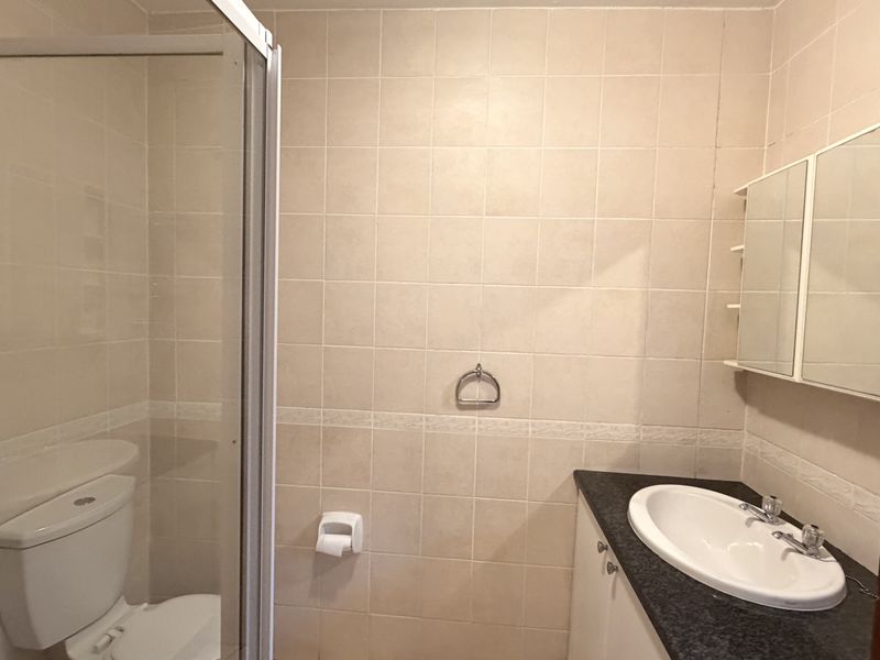 A functional bathroom featuring a shower enclosure, vanity cabinet with basin, and wall-mounted medicine cabinet, finished with neutral wall tiling.