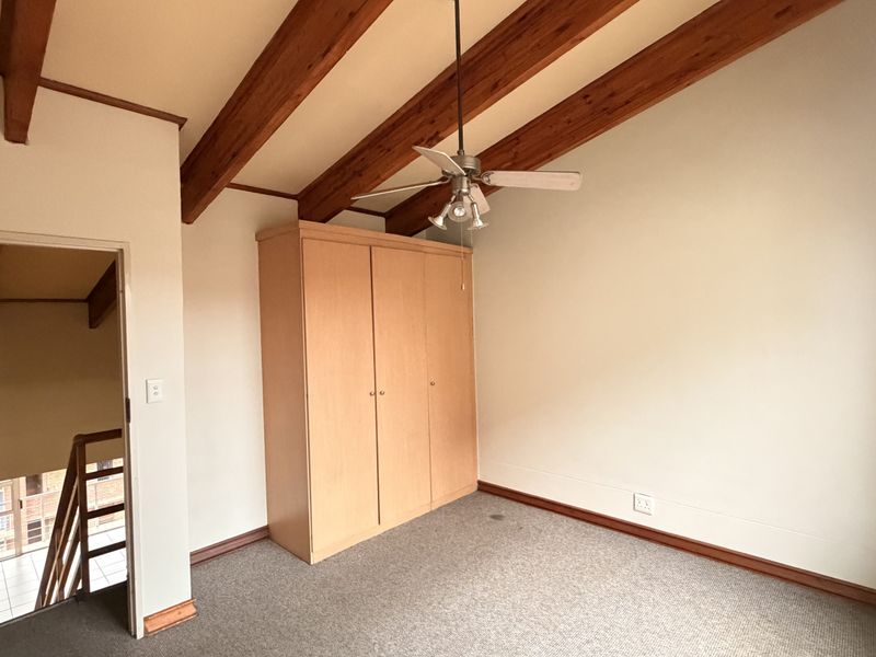 A spacious bedroom featuring exposed timber ceiling beams, a built-in wardrobe, and a ceiling fan, offering a neutral canvas for personalization.