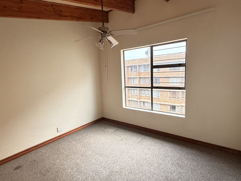 An empty bedroom featuring exposed timber ceiling beams, a ceiling fan, and a window with security bars.