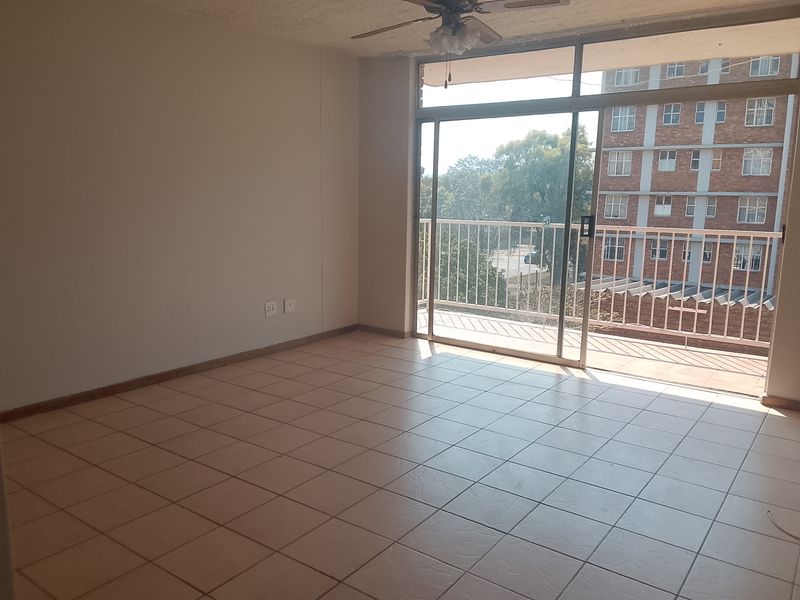 An empty living room featuring tiled flooring, a ceiling fan, and a large sliding glass door providing access to a balcony.
