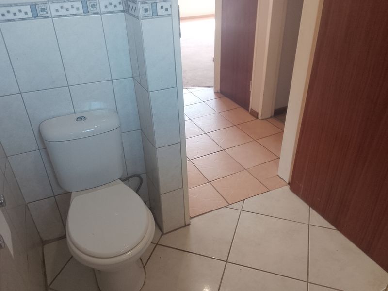 A functional bathroom featuring a standard toilet, tiled walls with decorative border, and ceramic floor tiling, leading into a hallway area.