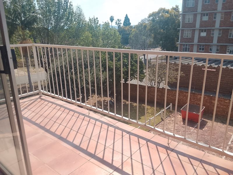 A simple balcony featuring tiled flooring and a metal balustrade, overlooking the apartment complex grounds and surrounding neighborhood.
