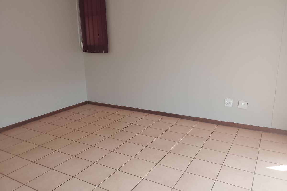 An empty bedroom featuring neutral tiled flooring, plain walls, and vertical window blinds.