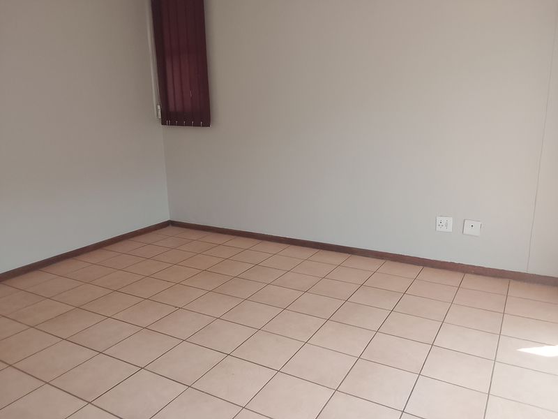 An empty bedroom featuring neutral tiled flooring, plain walls, and vertical window blinds.