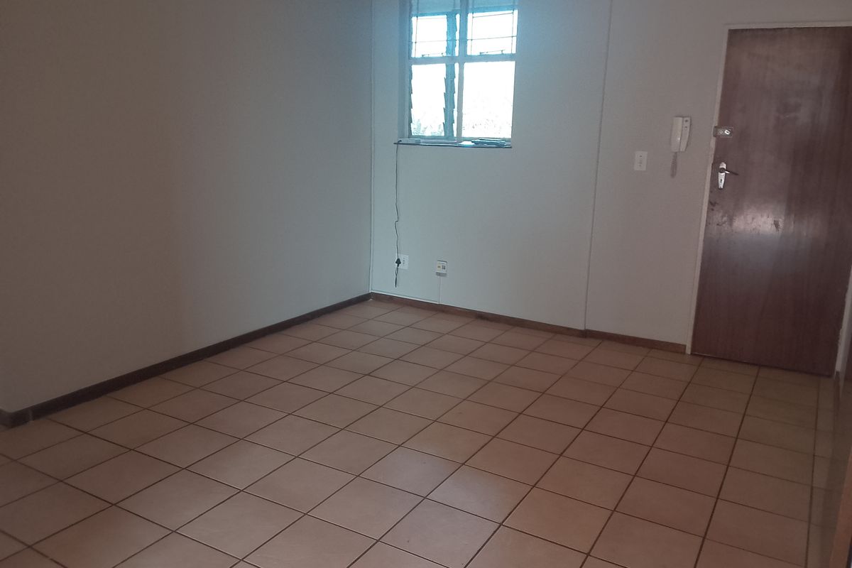 An empty living area featuring tiled flooring, a window with security bars, and an integrated intercom system.