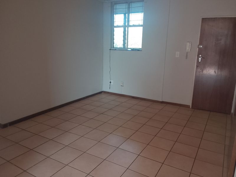 An empty living area featuring tiled flooring, a window with security bars, and an integrated intercom system.