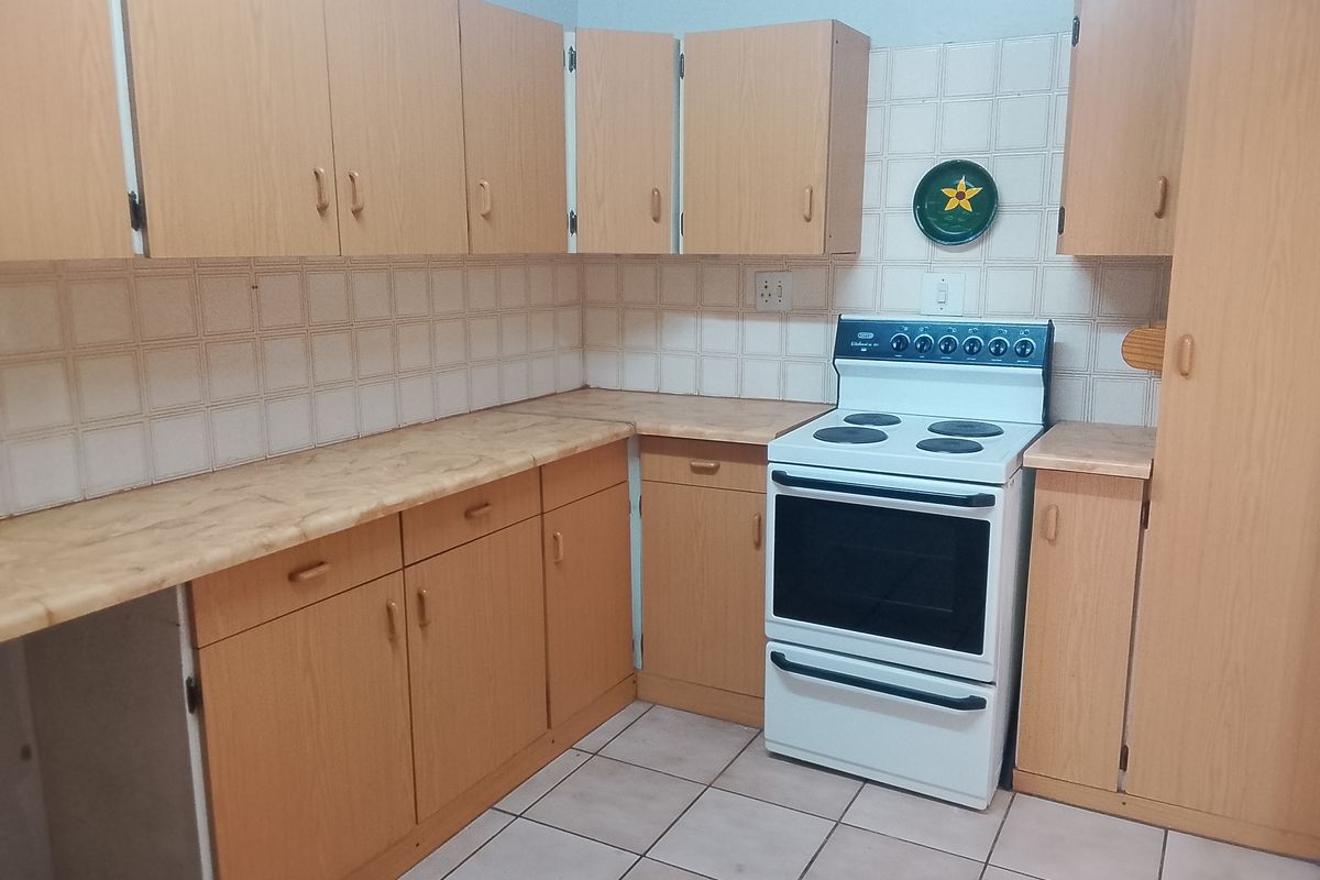 A functional kitchen featuring light wood-tone cabinetry, laminate countertops, ceramic tile backsplash, and a freestanding electric stove.