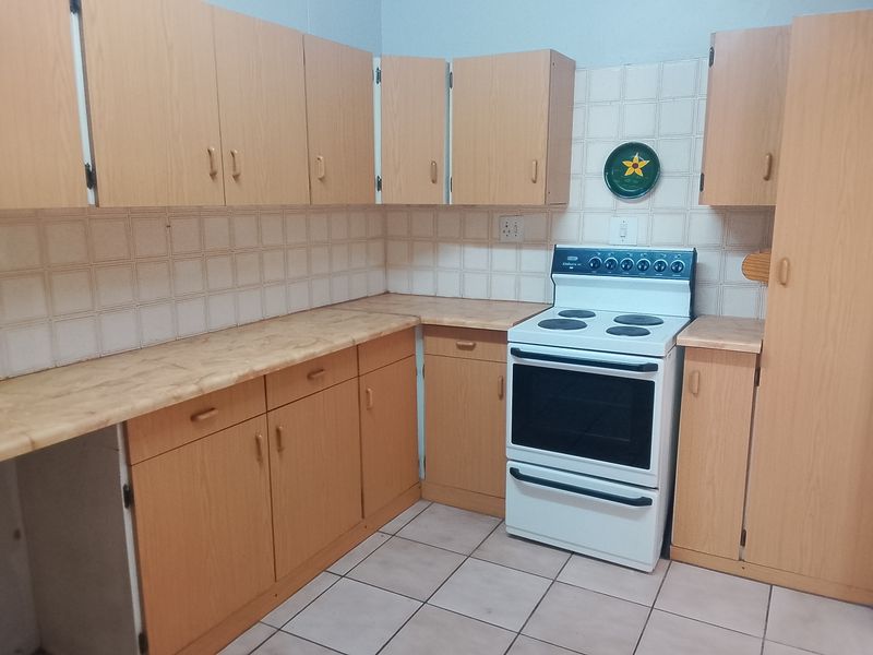 A functional kitchen featuring light wood-tone cabinetry, laminate countertops, ceramic tile backsplash, and a freestanding electric stove.