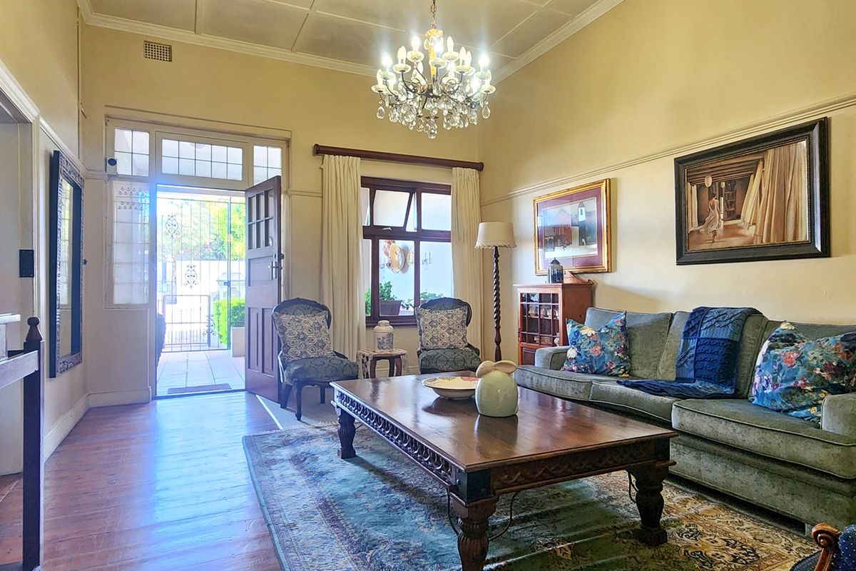 A well-maintained living room featuring original timber flooring, classic picture rails, and a decorative crystal chandelier, creating a warm and inviting atmosphere.