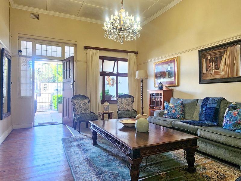 A well-maintained living room featuring original timber flooring, classic picture rails, and a decorative crystal chandelier, creating a warm and inviting atmosphere.