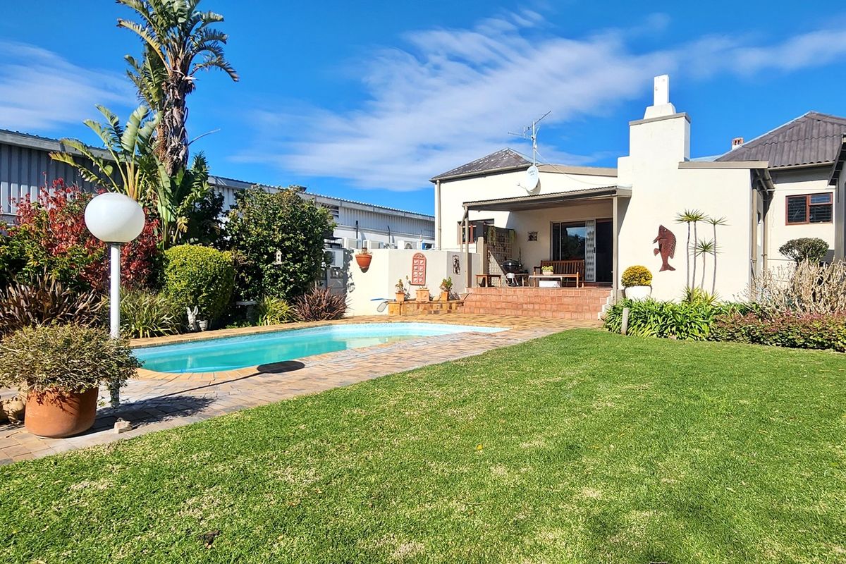 Rear exterior view featuring a swimming pool, brick patio area, and well-maintained lawn, providing a private outdoor entertainment space.