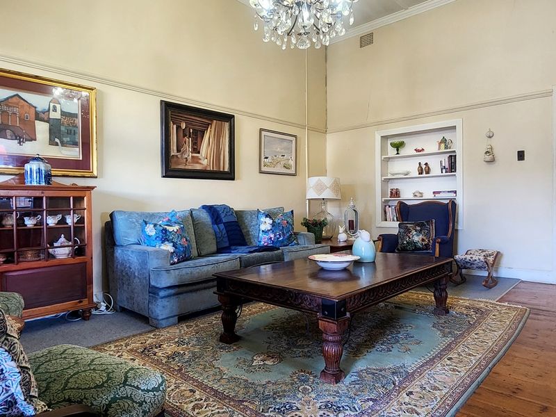 A spacious living room featuring classic timber flooring, picture rails, a built-in wall niche, and an elegant crystal chandelier.