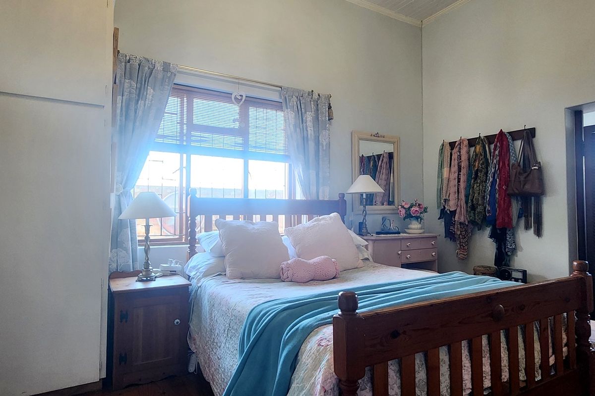 A bedroom featuring built-in cupboards and a window with timber frames, with an adjoining bathroom visible through the doorway.