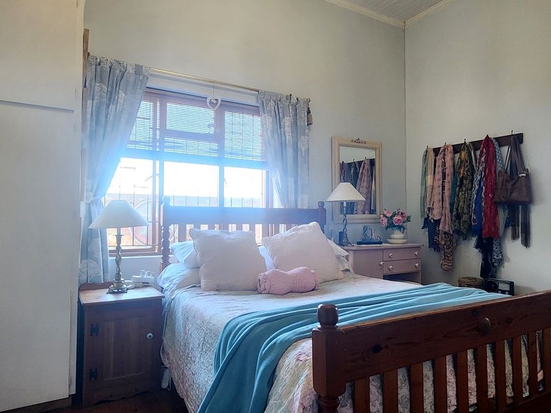 A bedroom featuring built-in cupboards and a window with timber frames, with an adjoining bathroom visible through the doorway.