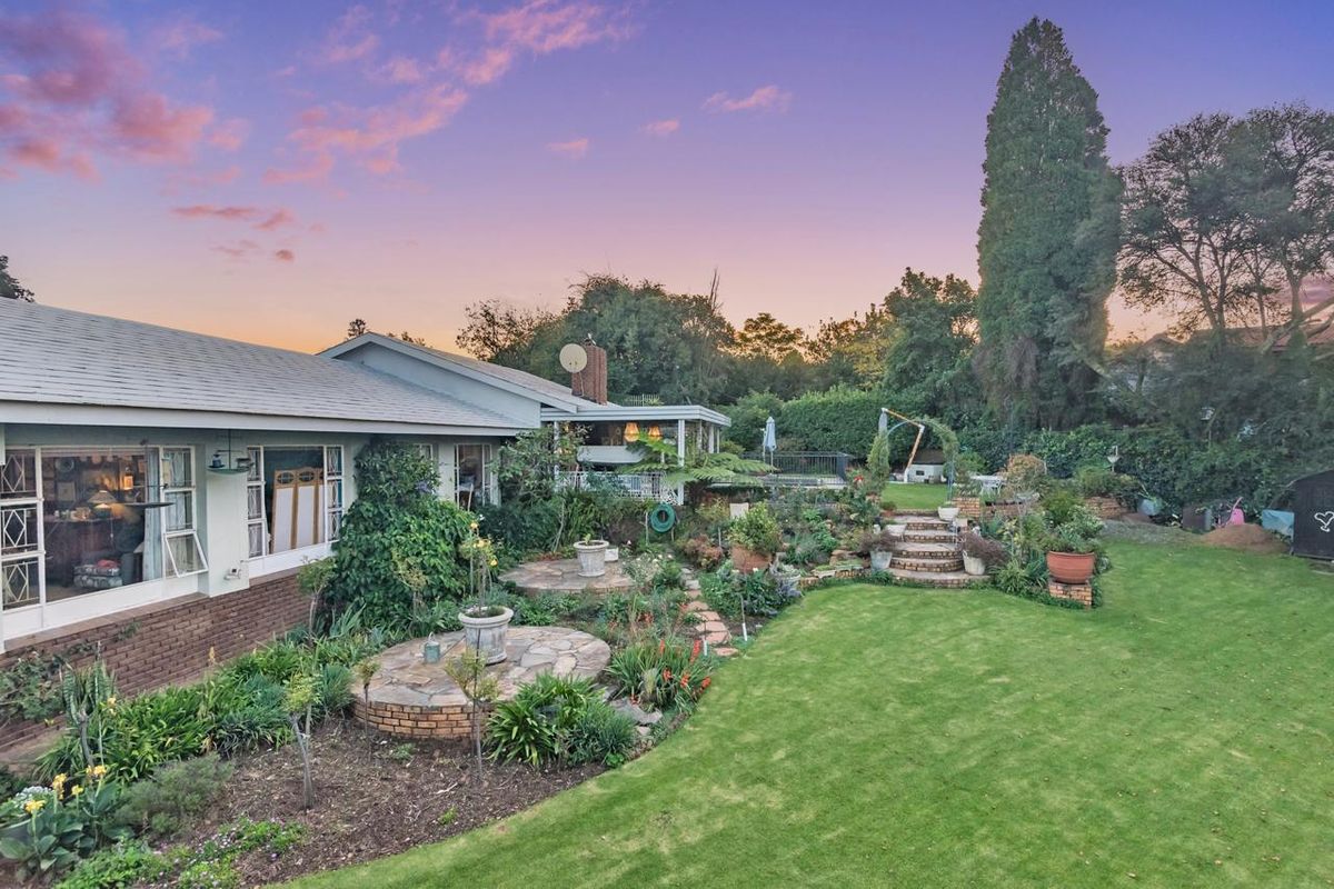 A spacious rear garden featuring a manicured lawn, stone patio areas, brick retaining walls, and established landscaping at sunset.