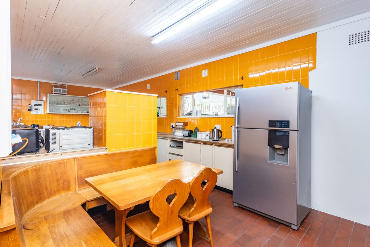 A dated kitchen featuring bright yellow wall tiles, timber ceiling, terracotta flooring, and built-in cabinetry with an integrated dining nook.