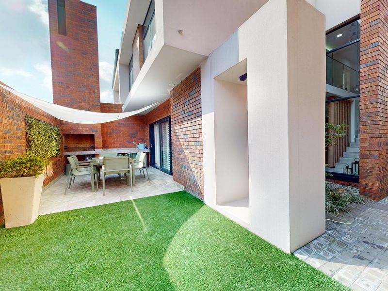 A modern outdoor patio area featuring a built-in braai, brick wall finishes, and a low-maintenance artificial lawn, perfect for outdoor entertaining.