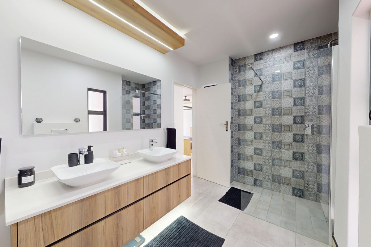 Modern bathroom featuring a double vanity with vessel sinks, floating cabinetry, and a spacious walk-in shower with decorative patterned wall tiles.