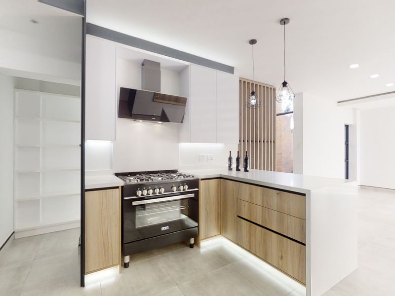 Modern kitchen featuring sleek white and wood-grain cabinetry, stone countertops, a gas stove with extractor fan, and integrated under-cabinet lighting.
