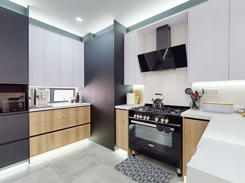 Modern kitchen featuring sleek two-tone cabinetry, high-end gas stove with extractor fan, stone countertops, and integrated under-cabinet lighting.