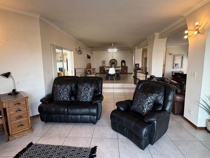 Spacious open-plan living and dining area featuring tiled flooring, neutral walls, and a stepped transition between the lounge and dining space.