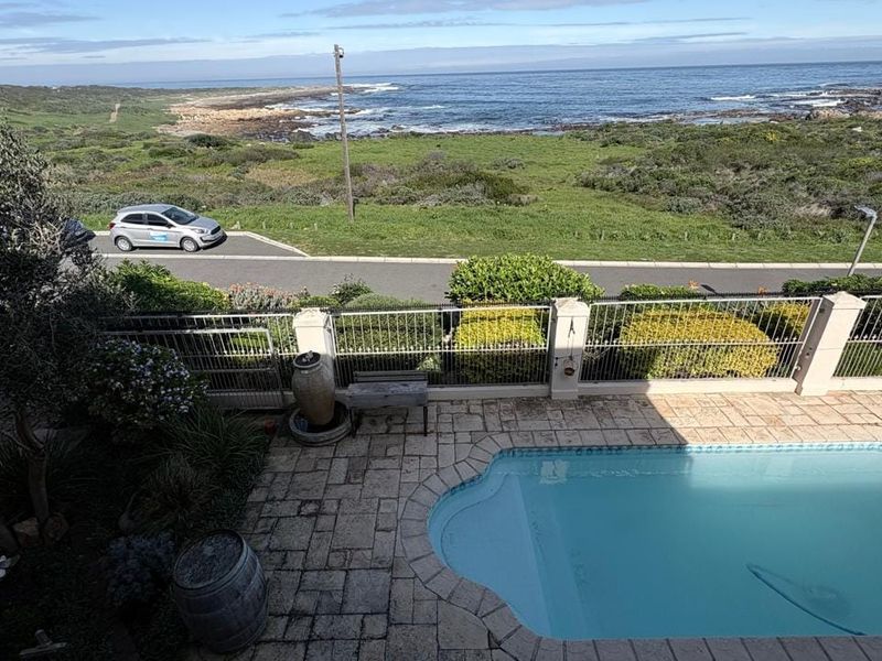 Outdoor pool area featuring a paved deck, metal fencing, and scenic coastal views overlooking the ocean.