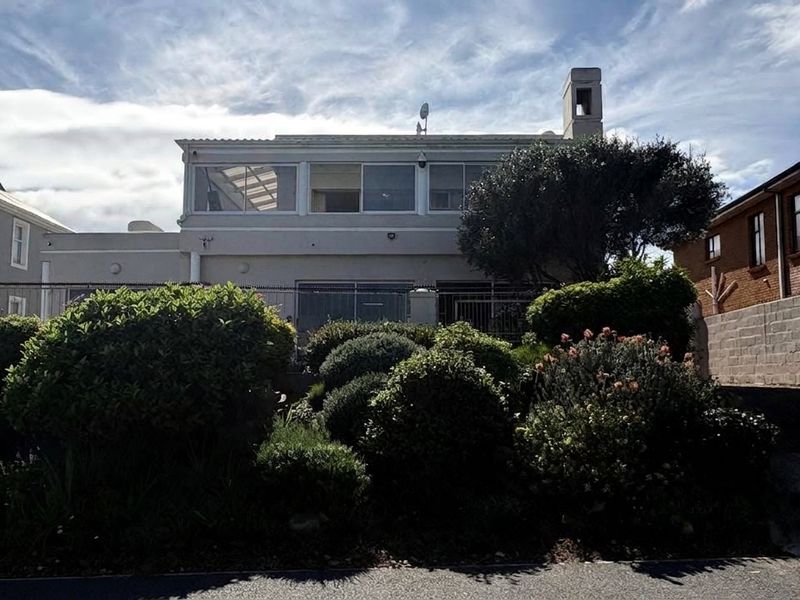 Front elevation of a multi-story house featuring an enclosed upper-level balcony, a prominent chimney, and a well-established front garden.