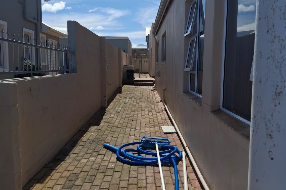 A narrow paved side passage or rear exterior walkway featuring boundary walls and access to the side of the property.