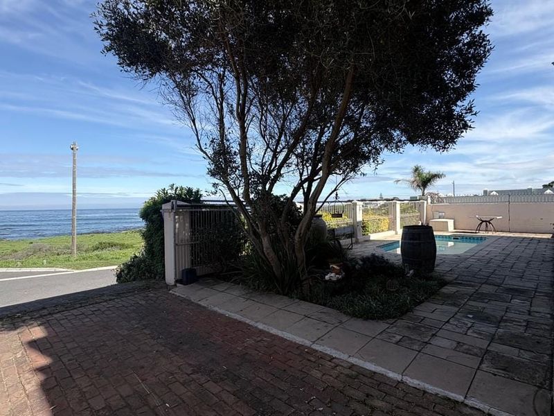 Outdoor pool area featuring a paved patio, boundary wall, and ocean views, providing a pleasant space for relaxation and entertainment.