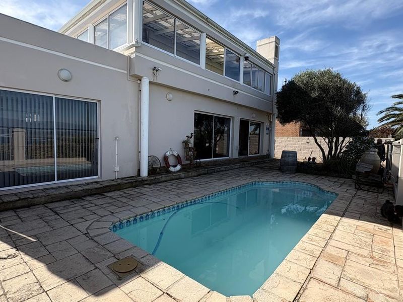 Rear exterior view featuring a swimming pool, stone paved patio area, and direct access to the home via sliding glass doors.