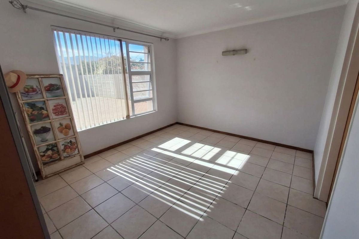 A bright, empty bedroom featuring neutral tiled flooring, a louver window with vertical blinds, and a wall-mounted light fixture.