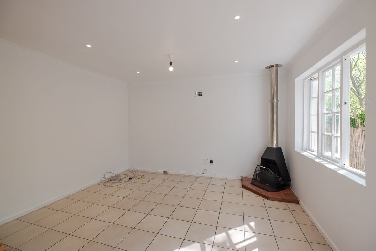 A bright, empty living room featuring neutral tiled flooring, recessed lighting, and a modern freestanding fireplace, offering a clean canvas for personalization.