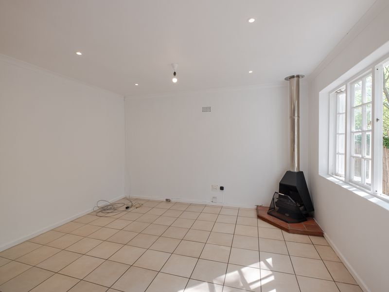 A bright, empty living room featuring neutral tiled flooring, recessed lighting, and a modern freestanding fireplace, offering a clean canvas for personalization.