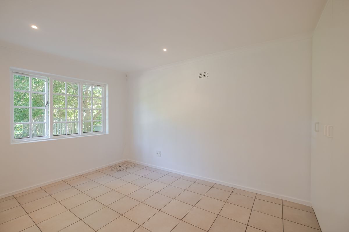 A bright, empty bedroom featuring neutral tiled flooring, recessed downlighting, and a built-in cupboard, offering a clean canvas for personalization.